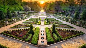 Un jardin symétrique avec un chemin central, bordé de parterres de fleurs et de haies soigneusement aménagés.