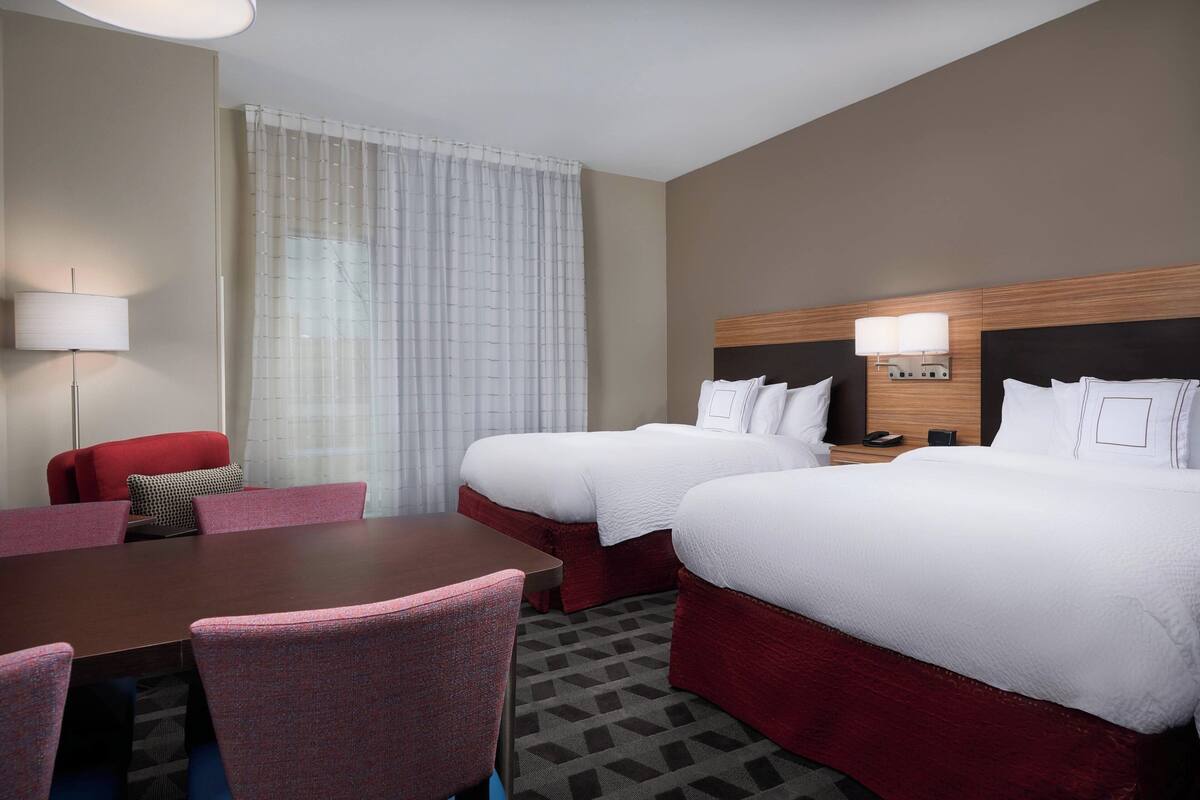 A hotel room with two beds, a desk, and a chair.
