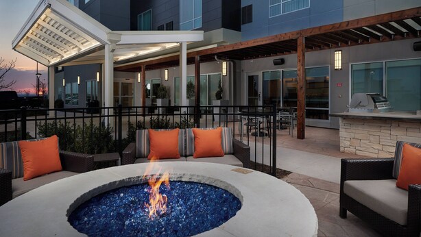 Un espace extérieur aménagé en terrasse, avec un foyer, des sièges et une partie couverte équipée d’un barbecue.