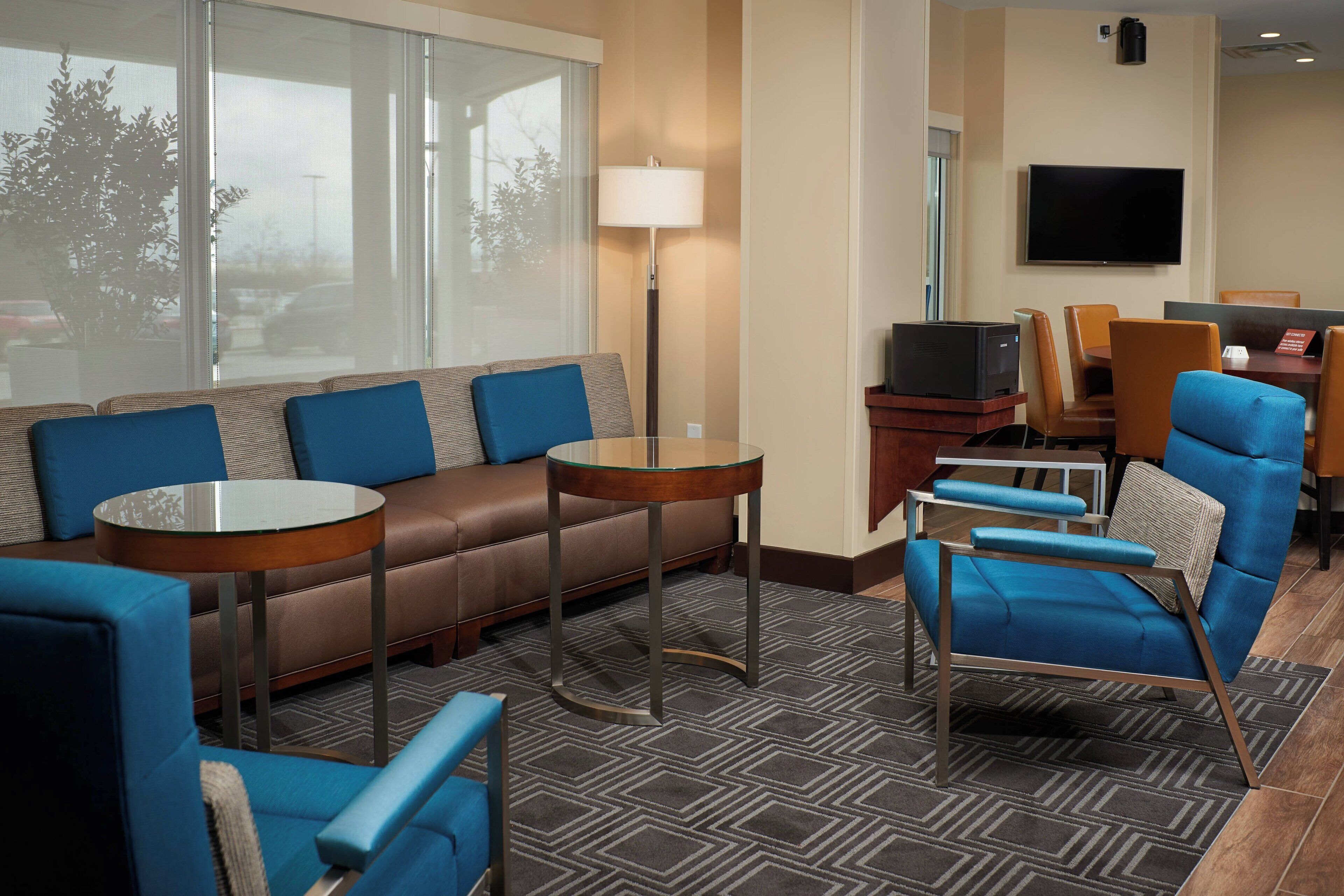 Een hotelkamer met een bank, fauteuils, een kleine tafel, een televisie en een bureau met stoelen.
