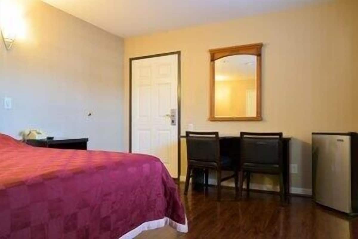 A hotel room with a bed, a desk, two chairs, a mirror, and a refrigerator.