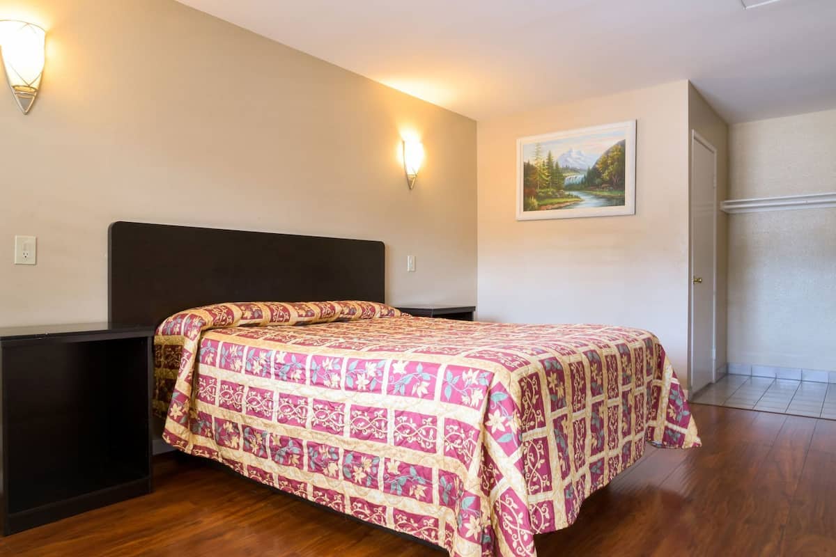 A bedroom with a bed, a nightstand, a wall-mounted light, and a painting.