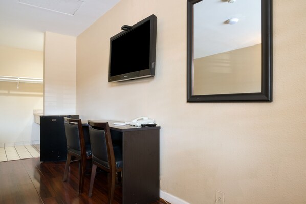 A small room with a desk, two chairs, a television mounted on the wall, a small refrigerator, and a mirror. - Covina Motel (West Covina)