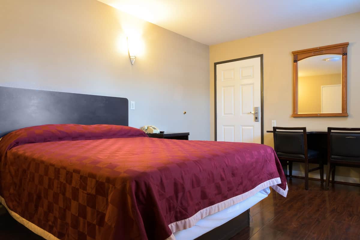 A hotel room with a large bed, a desk with two chairs, a door, and a mirror on the wall.
