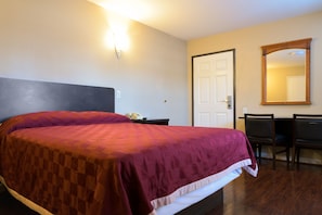 A hotel room with a large bed, a desk with two chairs, a door, and a mirror on the wall. - Covina Motel (West Covina)