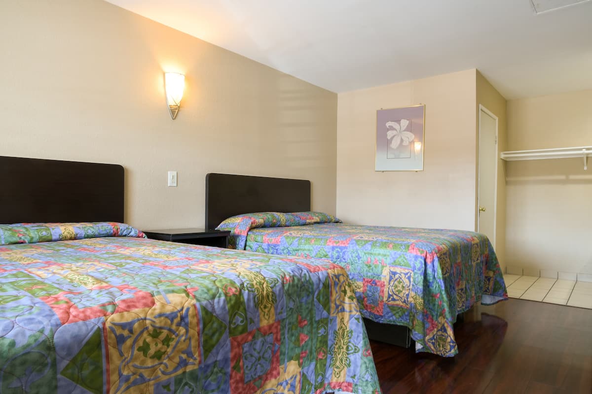 A room with two beds, each with a colorful quilt, a wall-mounted light, and a door.