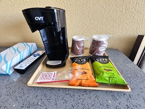 A coffee maker, two packets of coffee, a remote control, and a tray with a tissue box and a small packet of sugar. - Covina Motel (West Covina)