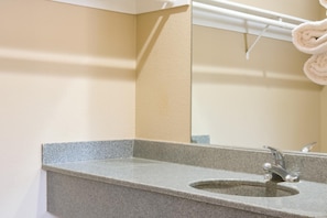 A bathroom with a granite countertop sink, a mirror, and a towel rack with rolled towels. - Covina Motel (West Covina)