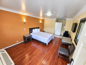 A hotel room with a bed, bedside table, chair, and a TV. - Covina Motel (West Covina)