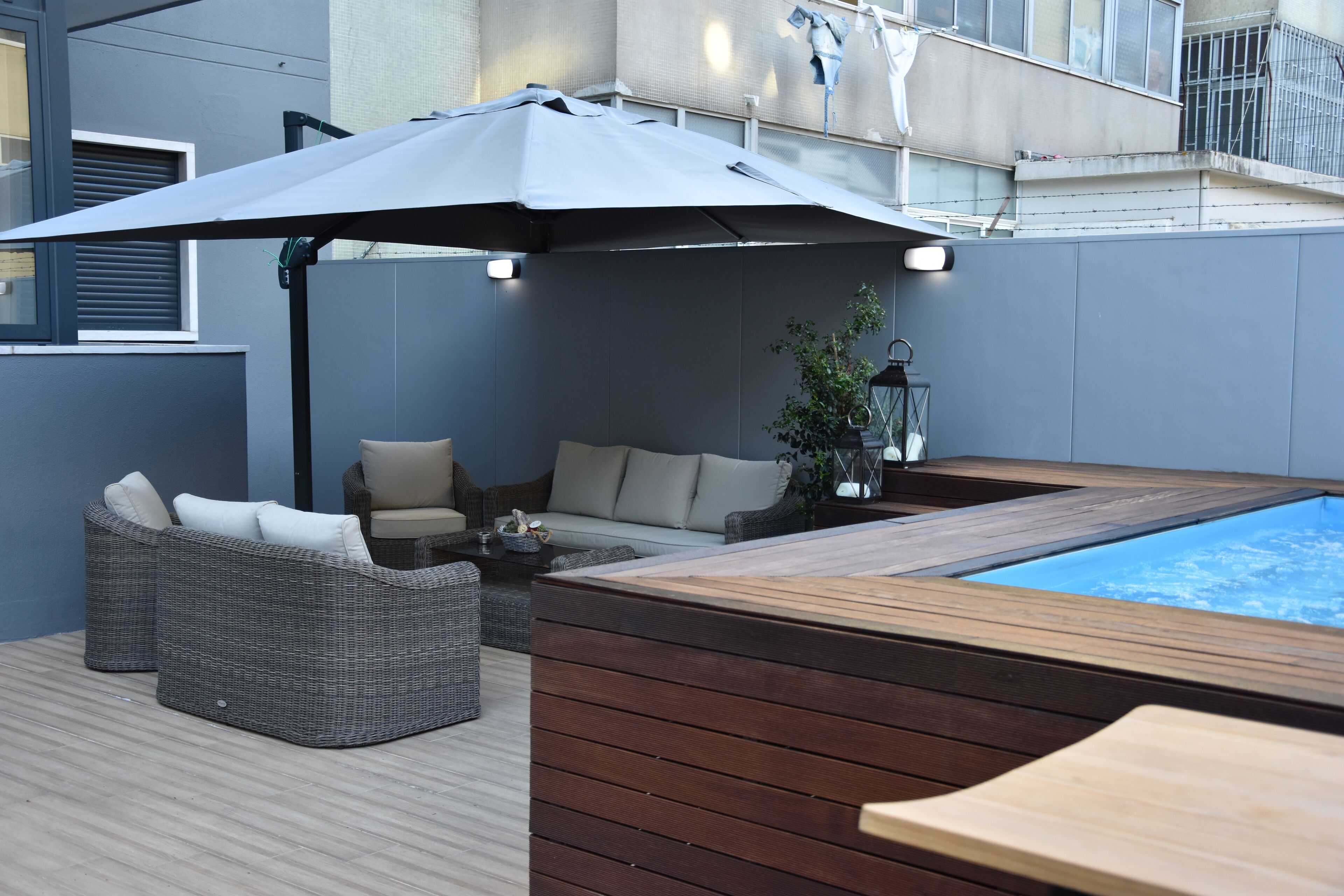 A rooftop terrace with a hot tub, wicker furniture, and a large umbrella providing shade.