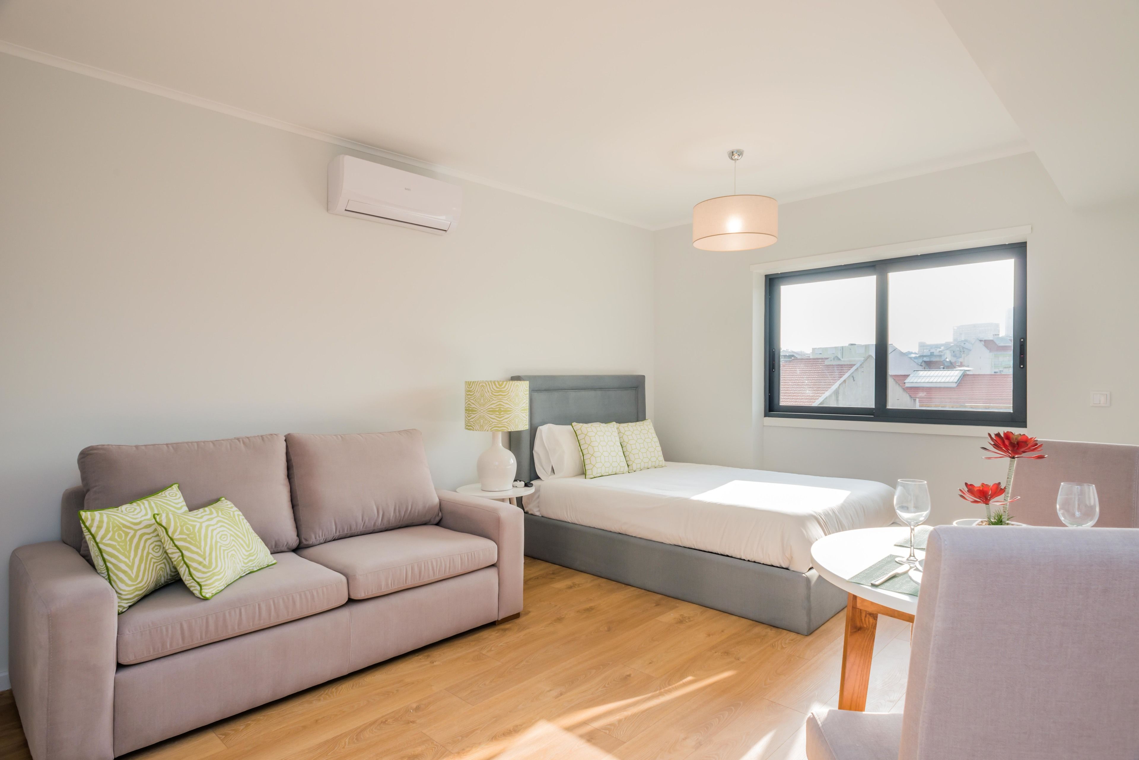 Une chambre moderne avec un canapé, un lit, une petite table et une fenêtre donnant sur la ville.