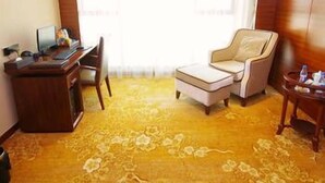A hotel room with a wooden desk, a computer, a chair, a small table with a bottle, and a large window. - Jun Hao Sunshine Hotel (Suining)