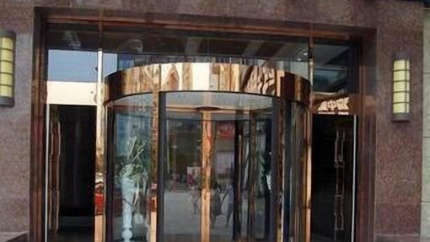 A revolving door entrance with a glass barrier, leading into a building with a brick facade and a large window. - Jun Hao Sunshine Hotel (Suining)