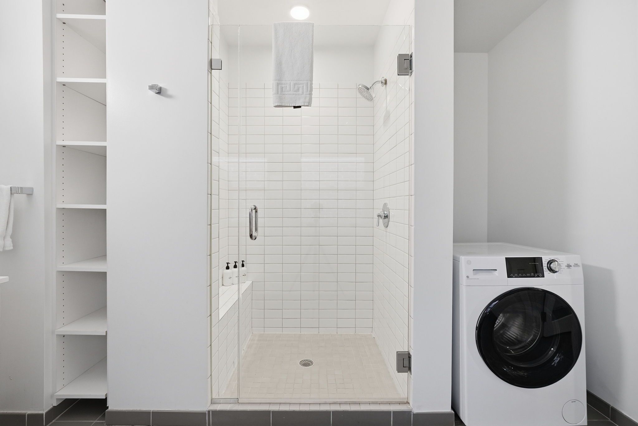 Un cuarto de lavado con lavadora, cabina de ducha y repisa con artículos de aseo.