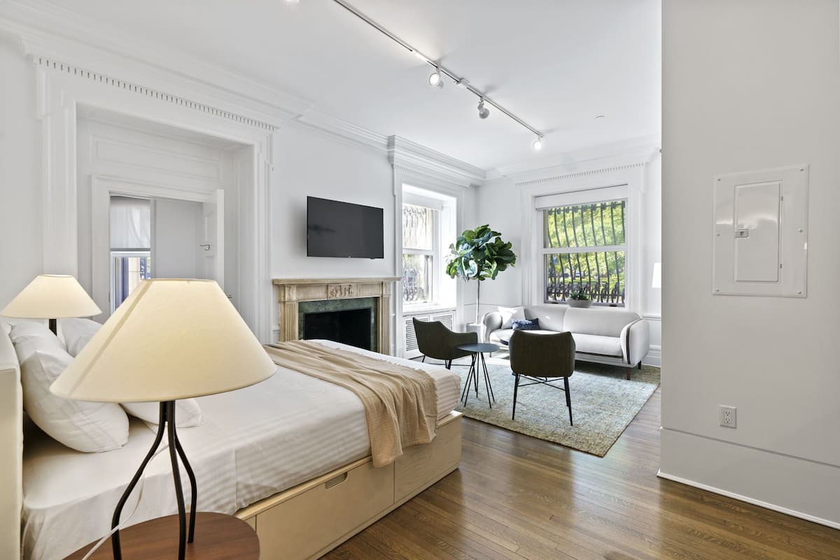 A modern bedroom with a bed, bedside lamps, a fireplace, a TV, and a seating area with a sofa and chairs.