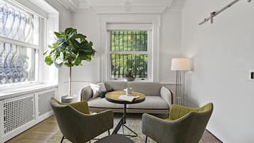 Ein Zimmer mit einer Couch, zwei Sesseln, einem Tisch, einer Lampe und einer großen Pflanze.