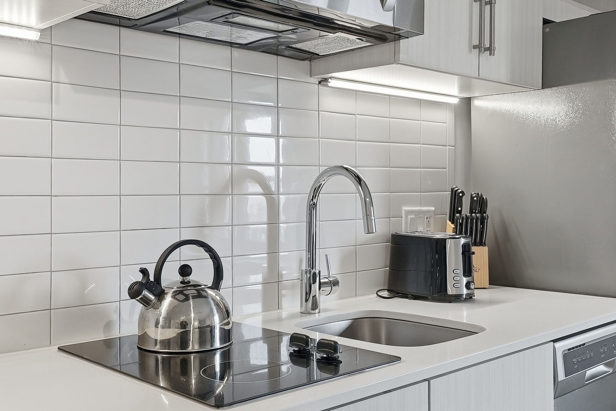 A modern kitchen with a stainless steel kettle, a toaster, and a sink.