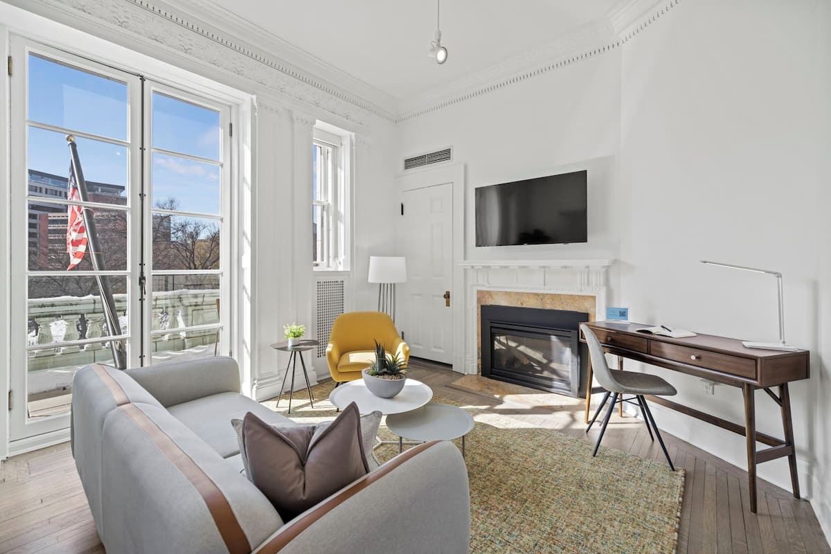 A living room with a sofa, a yellow armchair, a fireplace, a TV, and a desk.