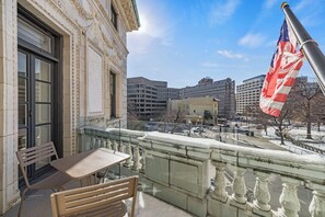 Een balkon met een tafel en stoelen, met uitzicht op een stadsbeeld met gebouwen en een Amerikaanse vlag.