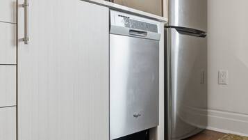 A stainless steel refrigerator and dishwasher in a kitchen with white cabinetry and a wooden floor.