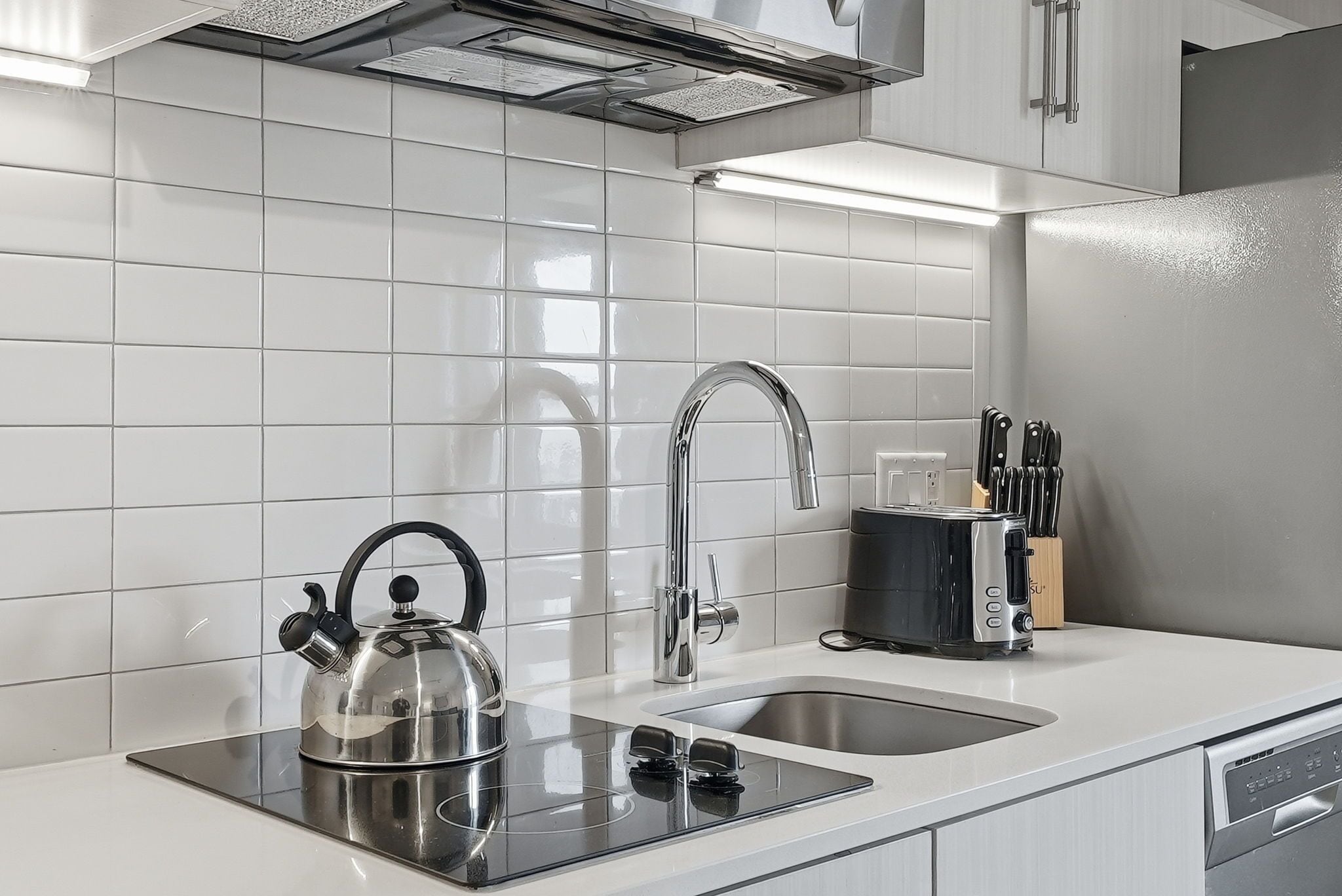 A modern kitchen with a stainless steel kettle, a sink, a toaster, and a knife block.