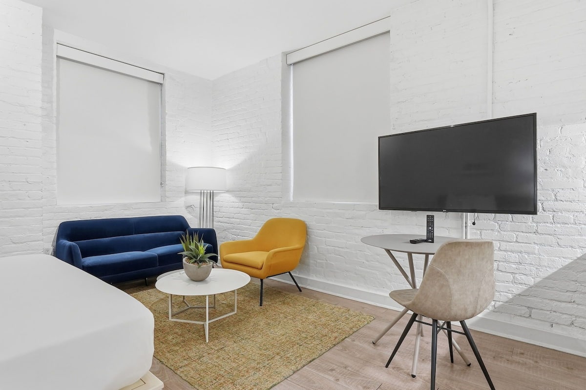 A modern living room with a sofa, armchairs, a TV, and a lamp.