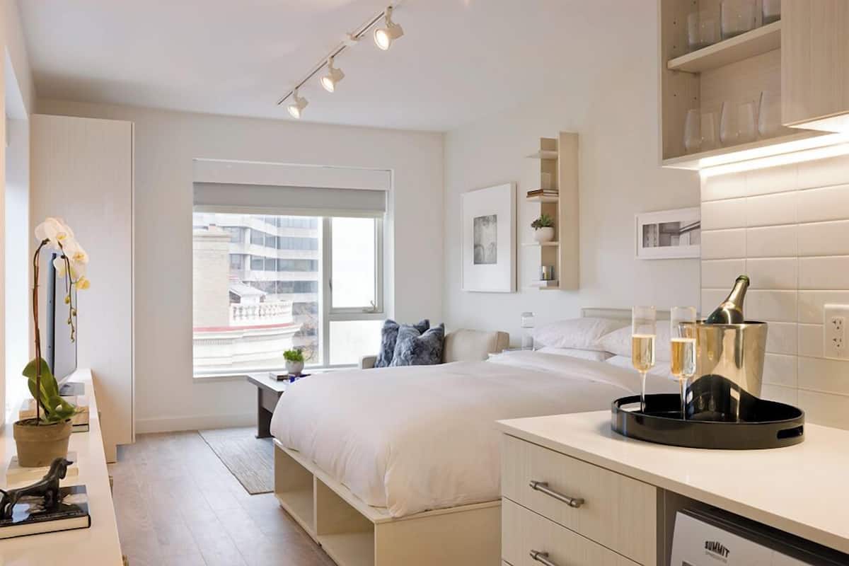 A modern hotel room with a bed, bedside table, and a view of the cityscape.