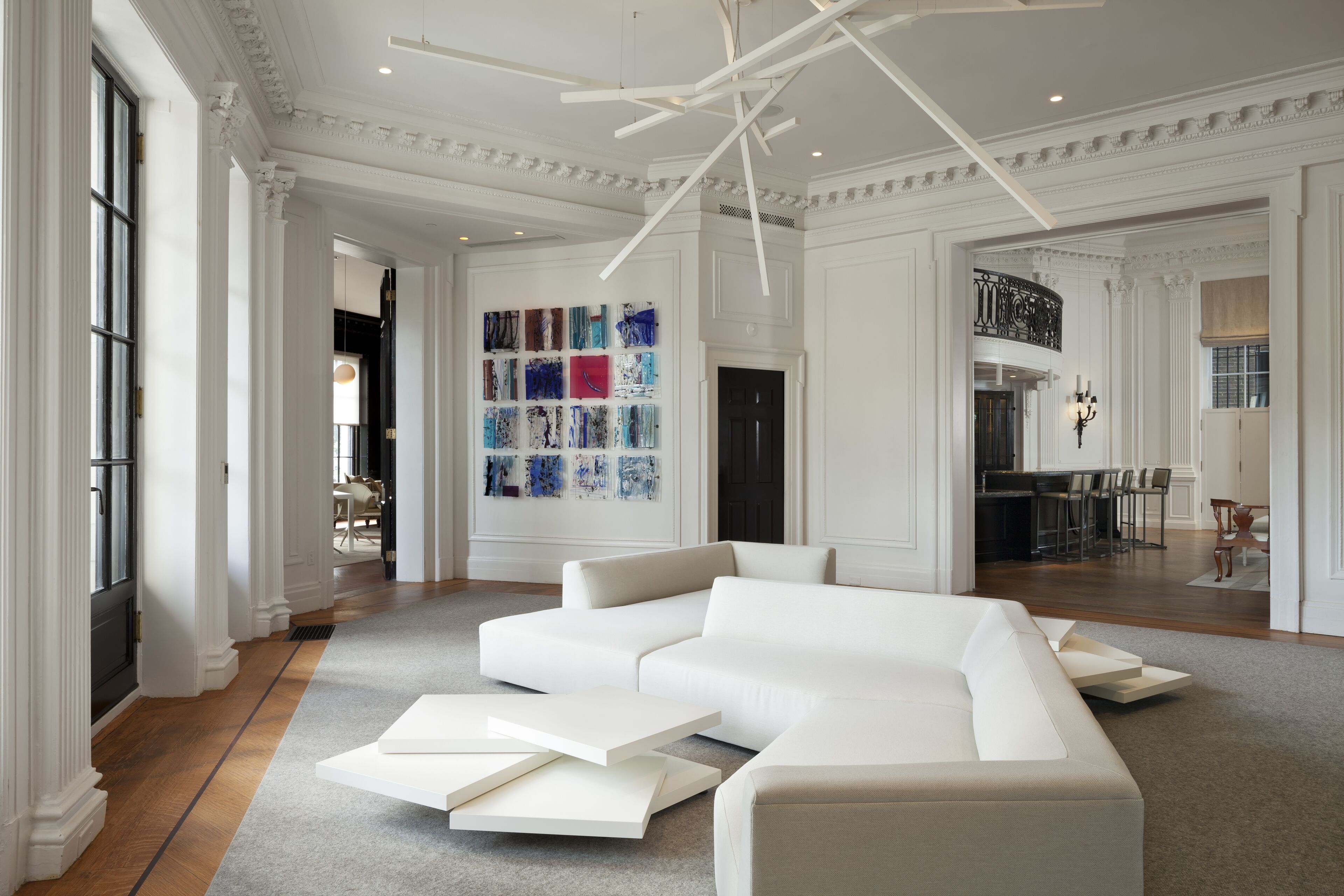 A spacious living room with a large white sectional sofa, a modern chandelier, and a wall of colorful abstract art.
