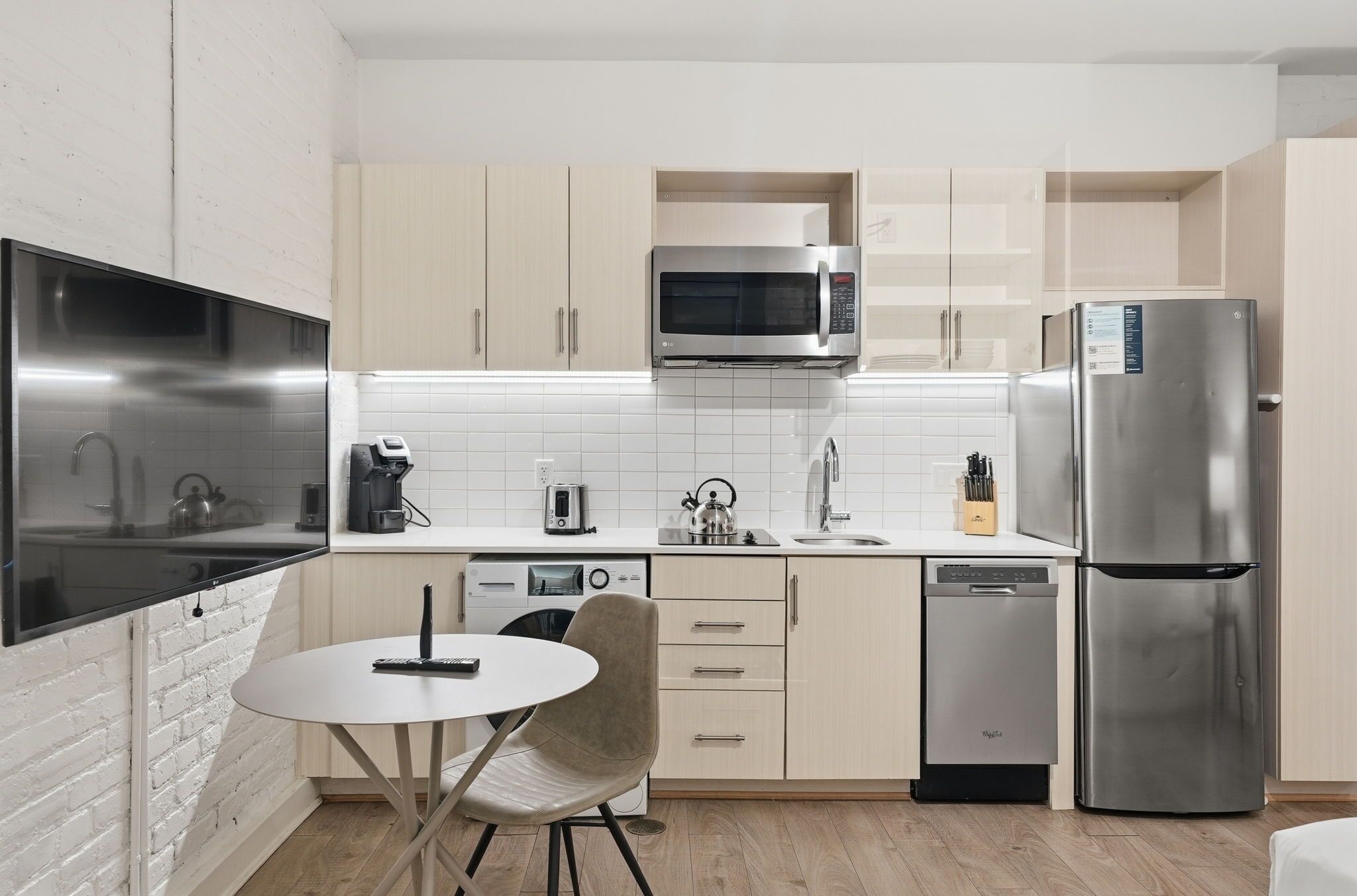 Una cocina moderna con televisor de pantalla plana, electrodomésticos de acero inoxidable, lavavajillas y comedor con una mesa redonda y una silla.