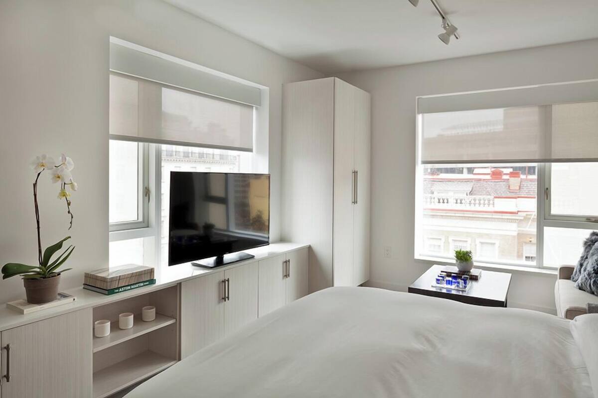 Een moderne slaapkamer met een bed, televisie, kastjes en een raam met uitzicht over de stad.