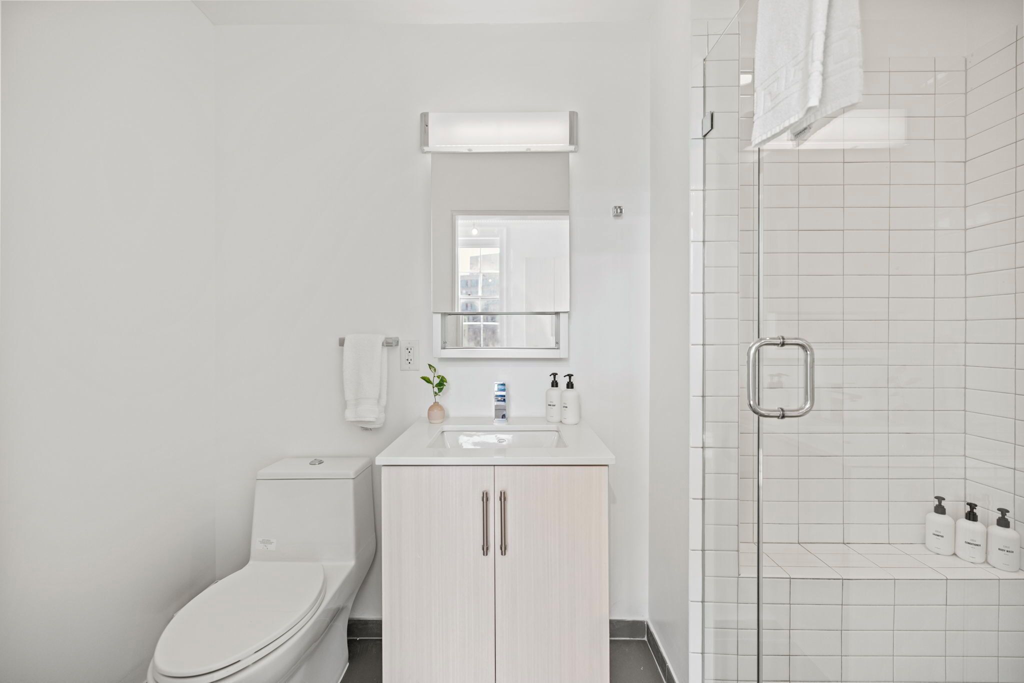 A modern bathroom with a toilet, sink, mirror, and shower area.