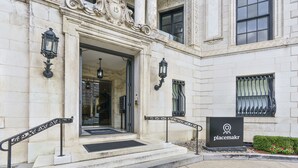 A building entrance with ornate columns, a black metal railing, and a placemat at the door. - Placemakr Dupont Circle (Washington)