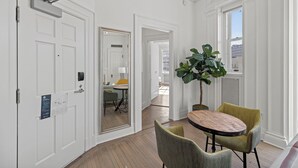 A room with a white door, a round table with two chairs, a large plant, and a view through a window. - Placemakr Dupont Circle (Washington)