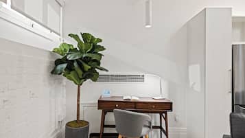 A compact, modern room with a wooden desk, a grey chair, a potted plant, and a white air conditioning unit.