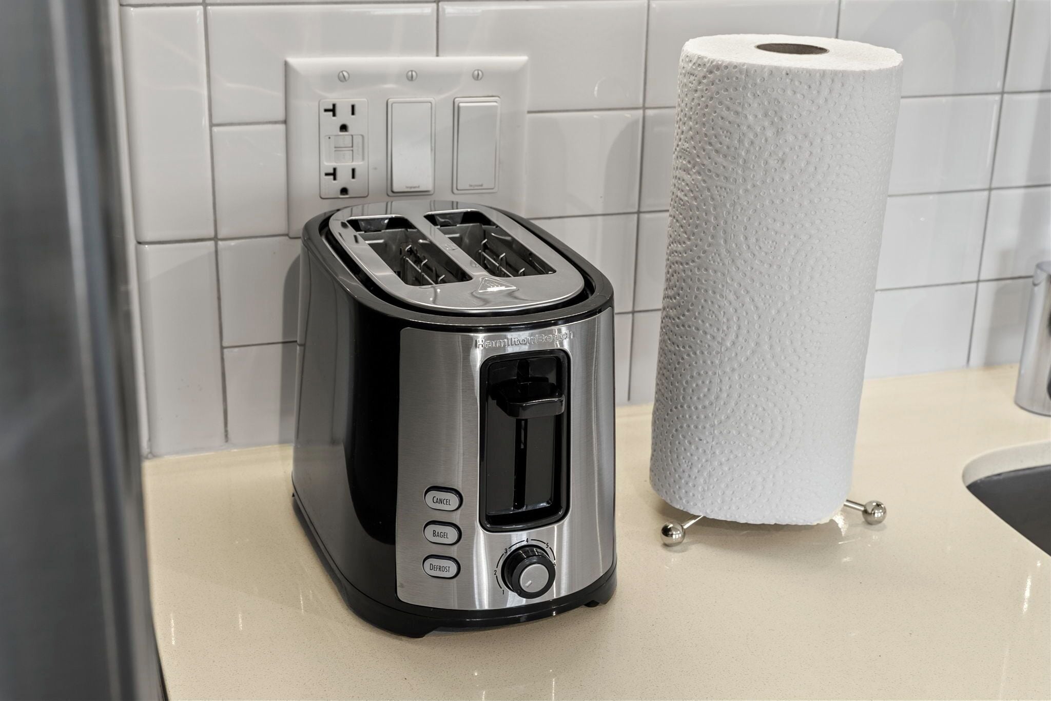 A kitchen with a toaster, a roll of paper towels, and a white tiled backsplash.