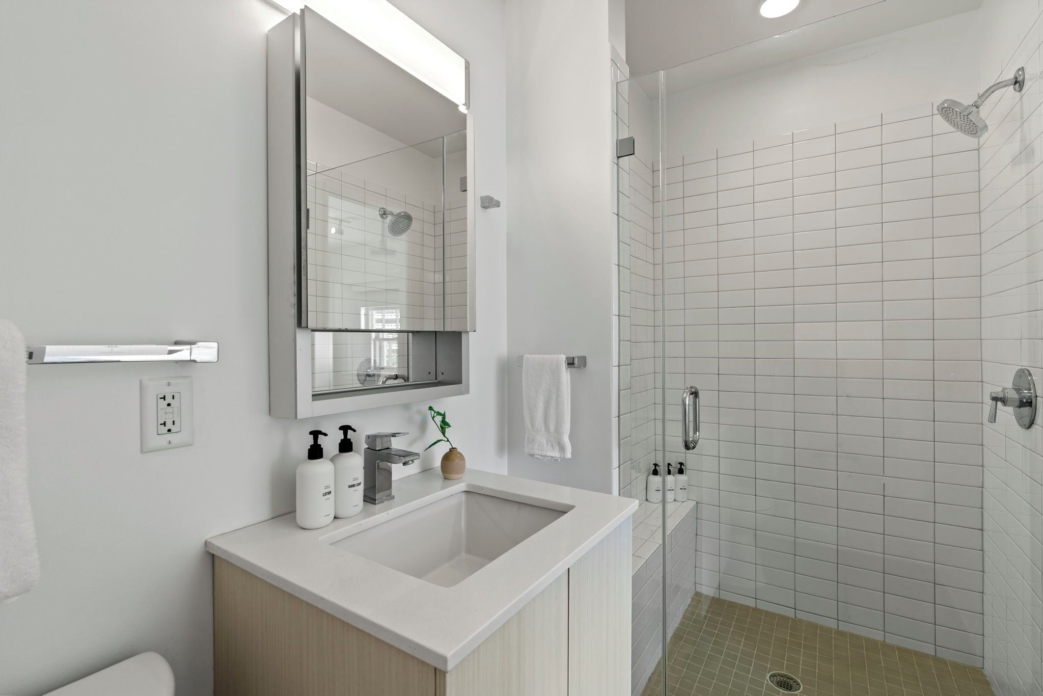 A modern bathroom with a large mirror, a sink, a shower, and a toilet.