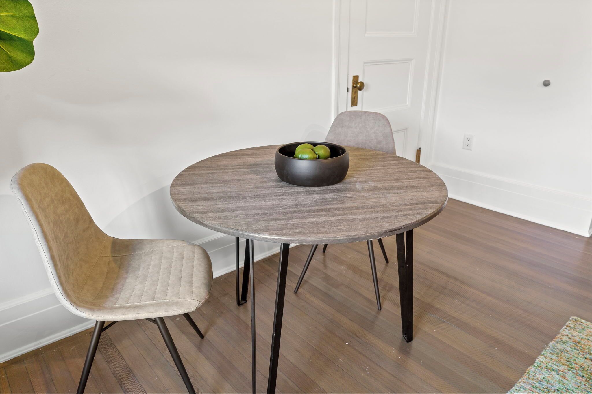 A dining table with a bowl of fruit, two chairs, and a door in the background.