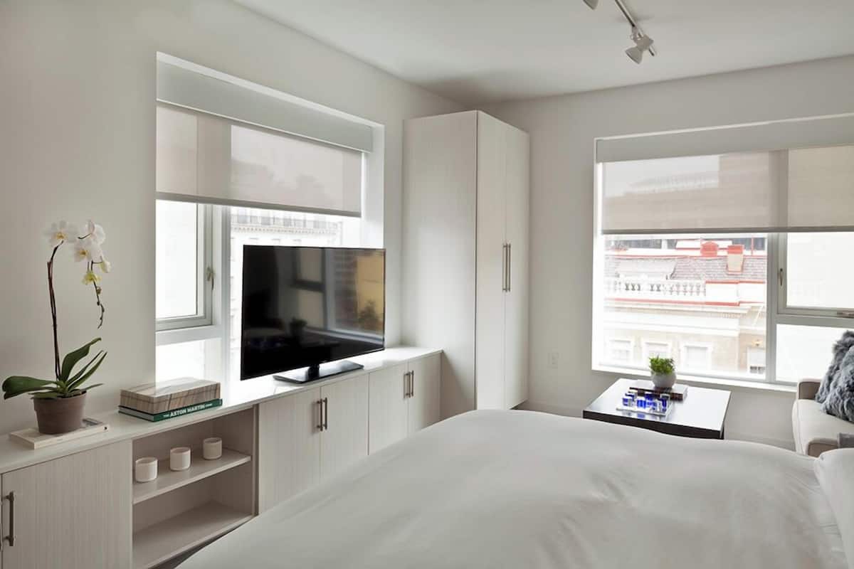 A modern bedroom with a bed, TV, cabinets, and a window with a city view.