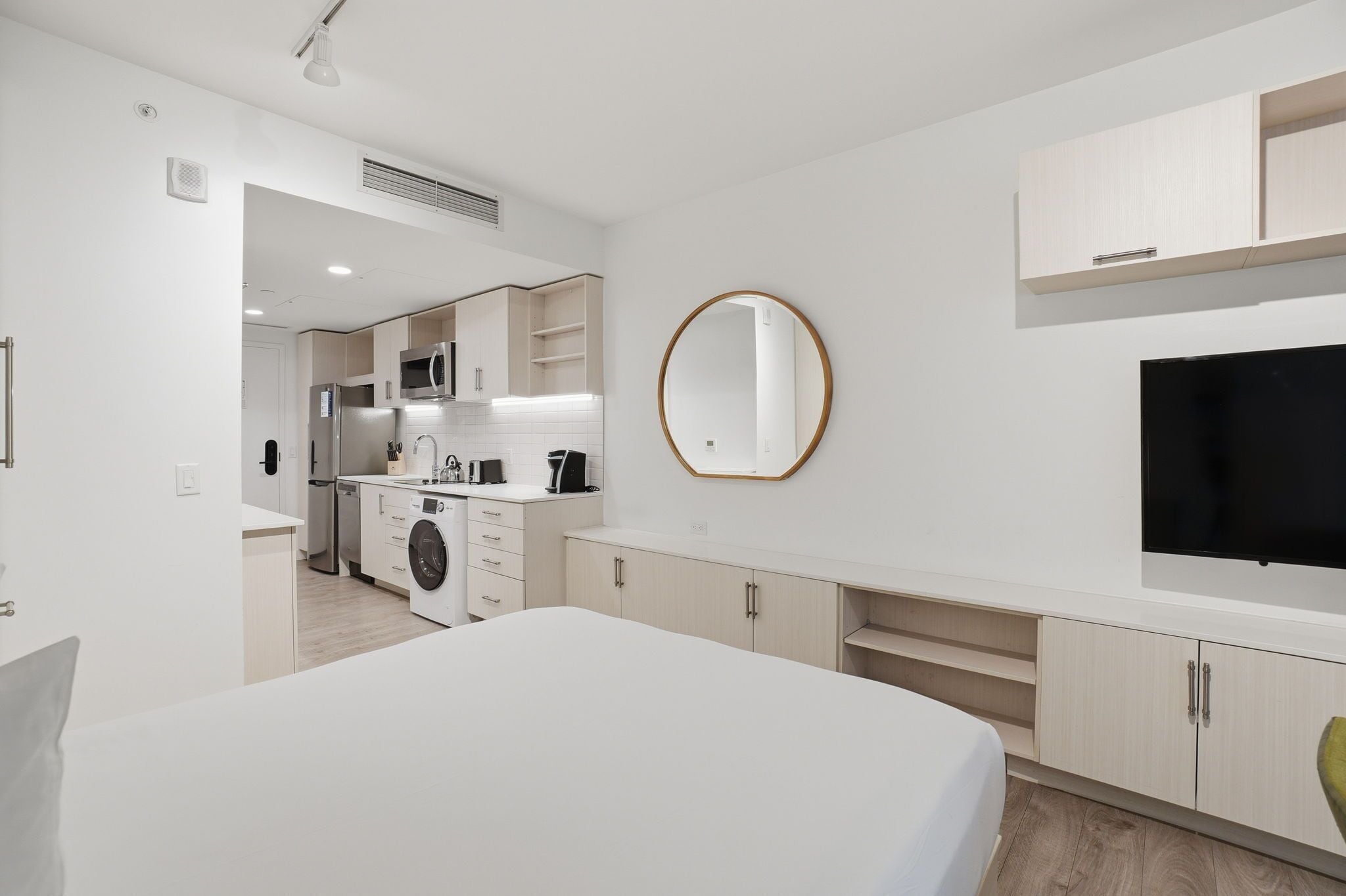 Una habitación de hotel moderna con una cama grande, televisión de pantalla plana, lavadora y kitchenette.