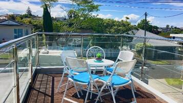 Un balcon avec une balustrade en verre, une table ronde avec quatre chaises et une petite plante en pot.