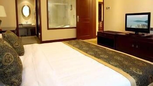 A hotel room with a large bed, a television, a dresser, and a bathroom visible through an open door. - Yingjia Resort (Lu'an)