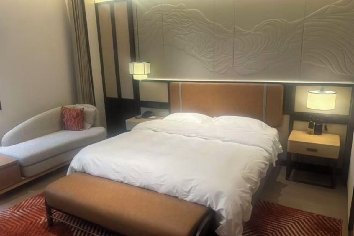 Una habitación de hotel con una cama, un sofá, una mesita de noche y una lámpara.