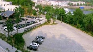 A parking lot with several cars, a building with a flat roof, and a river in the background. - Yingjia Resort (Lu'an)