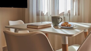 A table with a book, a mug, and a plate with pastries, a glass of water, and a TV mounted on the wall. - "Votsalo" deluxe studio - Studio apt / Sea view /Shared Pool / Sleeps 3 (Malevizi)