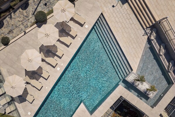 A rectangular swimming pool with lounge chairs and umbrellas, surrounded by a tiled deck.