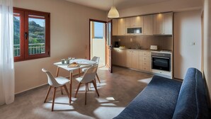 A modern kitchen with wooden cabinets, a dining area with a table and chairs, and a sofa. - "Votsalo" deluxe studio - Studio apt / Sea view /Shared Pool / Sleeps 3 (Malevizi)