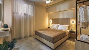 A modern hotel room with a large bed, a ceiling fan, a bedside table with a lamp, a mirror, and a wardrobe. - "Ilios" apartment - 1 Bedroom Apt / Sea view /Shared Pool / Sleeps 4 (Malevizi)