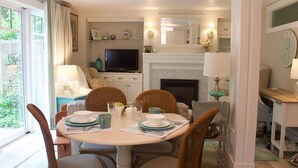 A dining area with a round table, chairs, and a television in the background. - Charming cottage apartment, private, quiet and sparkling clean.  1 bedrm 1 bath. (Kennebunk)