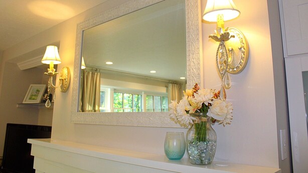 A bathroom vanity with a mirror, two wall sconces, a vase with flowers, and a blue glass container. - Charming cottage apartment, private, quiet and sparkling clean.  1 bedrm 1 bath. (Kennebunk)