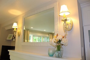 A bathroom vanity with a mirror, two wall sconces, a vase with flowers, and a blue glass container. - Charming cottage apartment, private, quiet and sparkling clean.  1 bedrm 1 bath. (Kennebunk)
